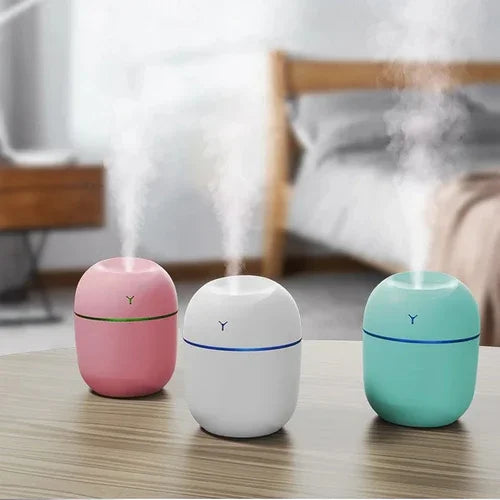 Three colorful portable humidifiers misting on a table in a modern bedroom setting